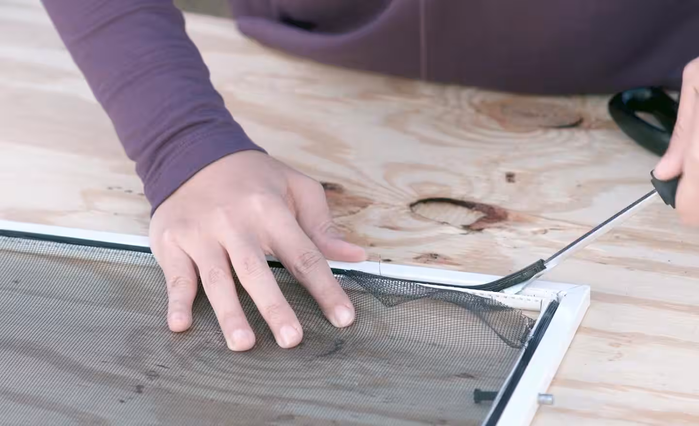 Hands securing replacement mesh into a window screen frame